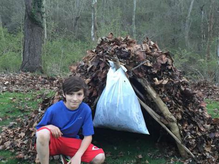 Boy sitting in front of a hut made of leaves with a trash bag hanging from it